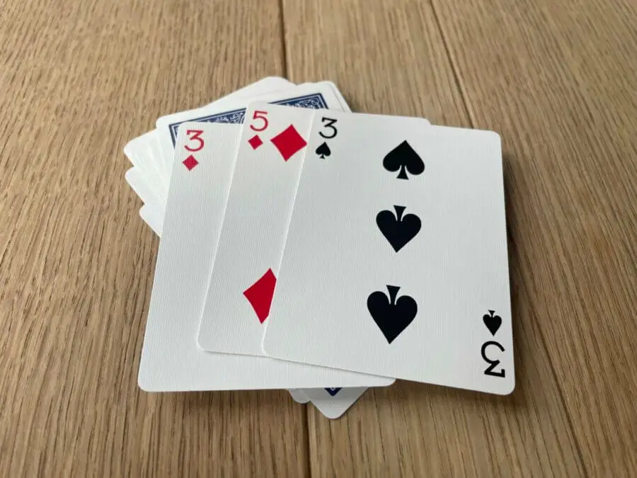 A set of three cards being revealed on a deck of cards, showing two 3's and a 5